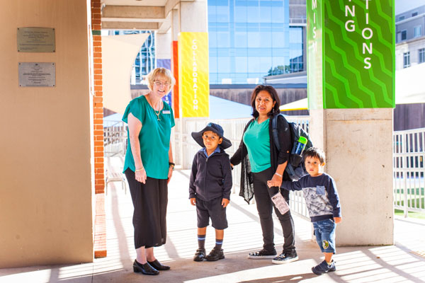 Mother and her two children standing in the school grounds with a staff member