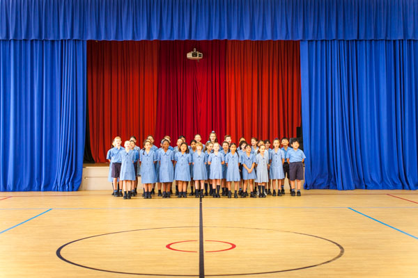 Students singing in front of a stage with a bright blue and red backdrop