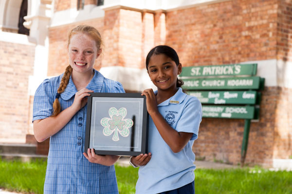 Two students smiling and holding up framed artwork of a shamrock